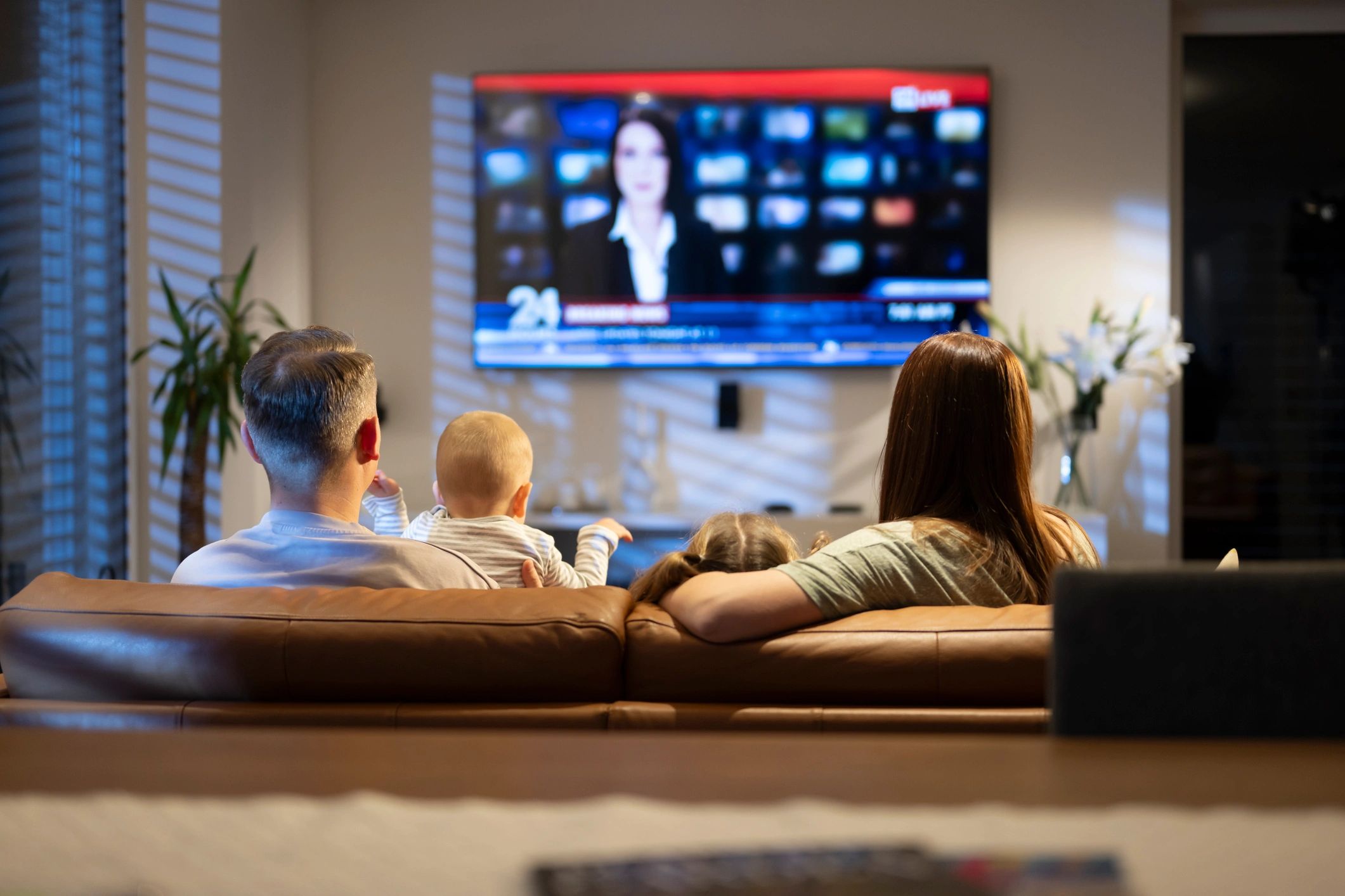 Modern Family Watches Evening News Together on Brown Leather Sofa in Cozy Living Room